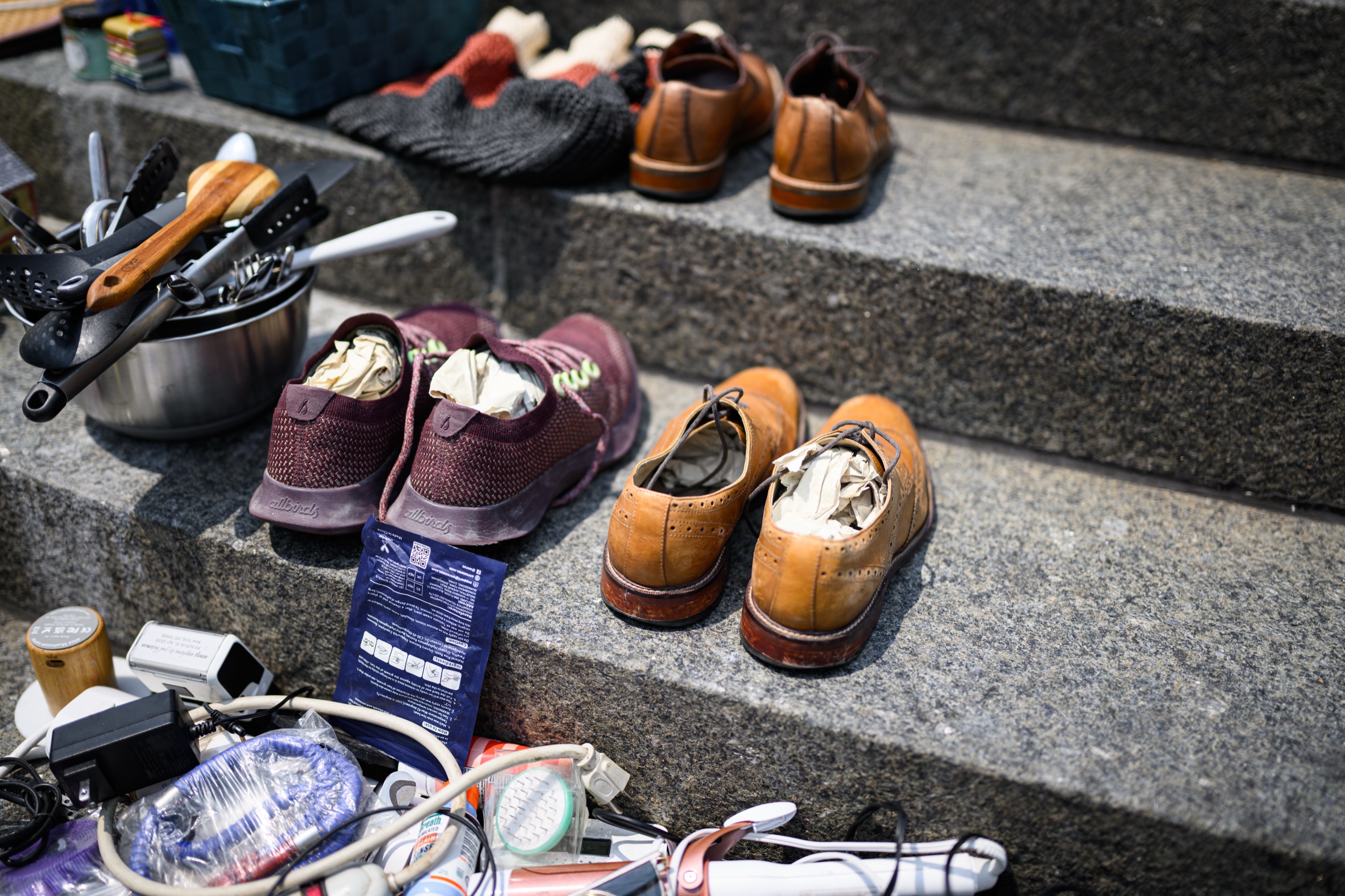 Used shoes, kitchen utensils, and household goods arranged on the sidewalk