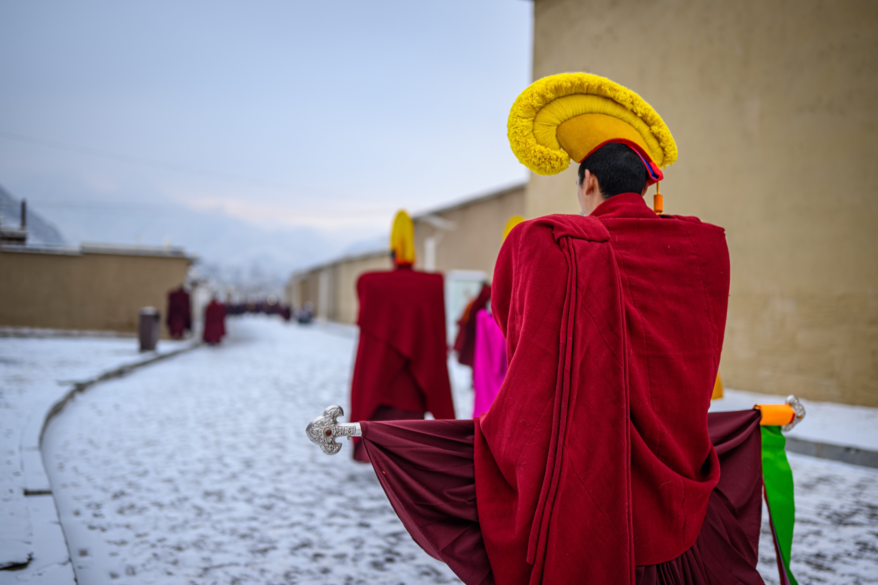 A monk in red robes and a yellow ceremonial hat seen from behind